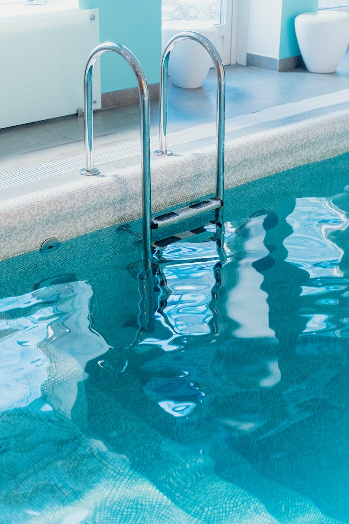 heros-img A serene view of an indoor swimming pool with a metal ladder and clear water.